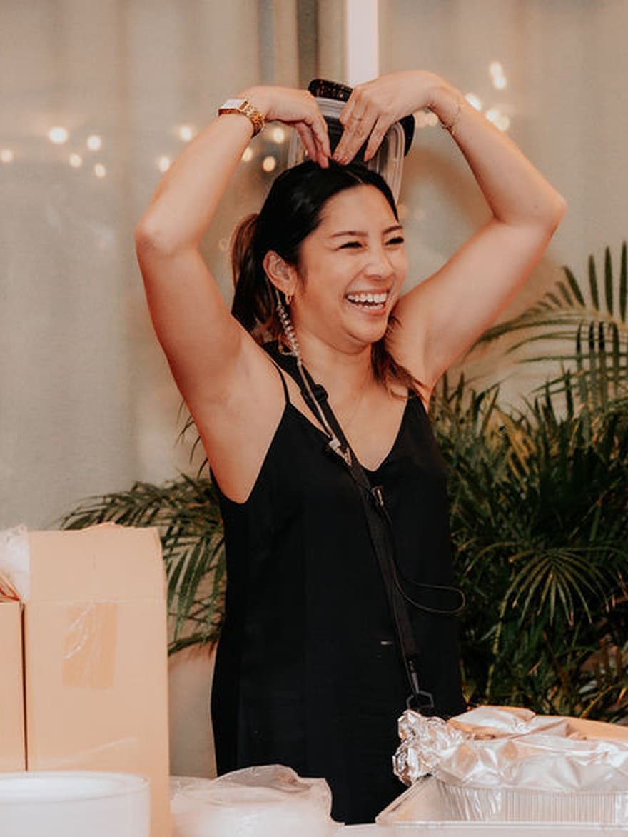 Lauren Fujimoto laughing with her arms raised while coordinating a wedding reception